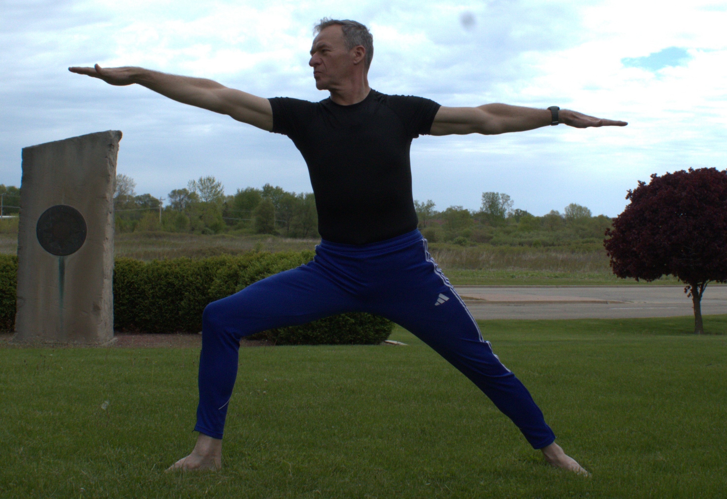 Roy in a focused outdoor Warrior Two yoga pose
